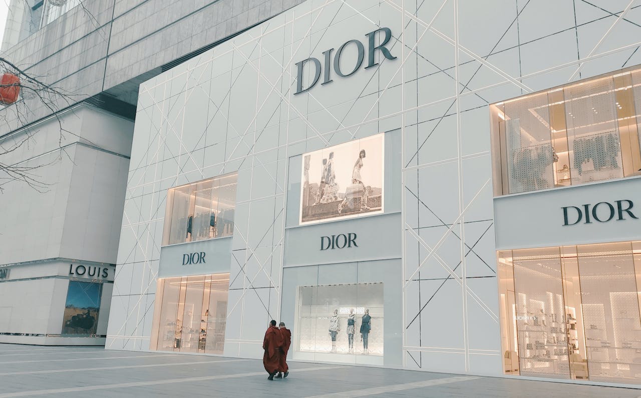 Elegant Dior storefront against urban backdrop featuring window displays and shoppers.